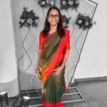 a girl wearing specs, standing and smiling, wearing saree